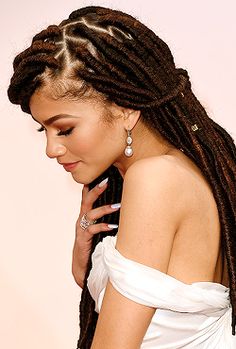 a woman with dreadlocks is wearing a white dress and holding her hand to her ear