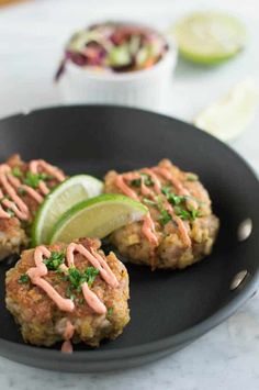 three crab cakes on a black plate with lime wedges and garnishes