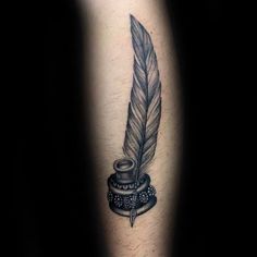 a black and white tattoo with a feather on top of a ink pot, next to a quill