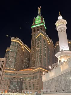 the clock tower is lit up at night in front of some tall buildings with lights on them