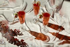 three glasses filled with red wine and garnish on a white table cloth next to silverware