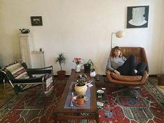 a woman sitting in a chair on top of a rug next to a coffee table