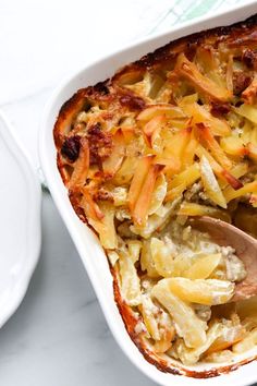 a casserole dish with potatoes and meat in it on a white plate next to a wooden spoon