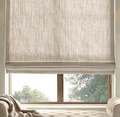 a living room with a couch and window covered in white roman blind shades on the windowsill