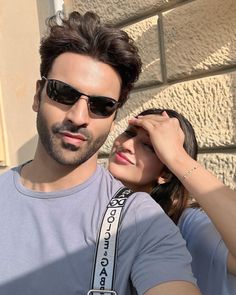 a man and woman standing next to each other near a brick wall with sunglasses on