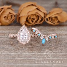 an engagement ring with a pear shaped center surrounded by blue and white stones sits on a wooden surface next to roses