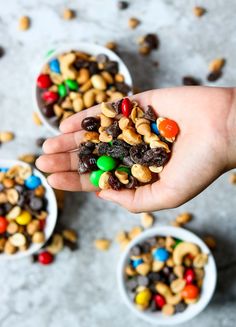 someone is holding their hand full of candy and cereals in small white bowls on the floor