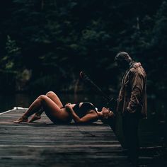 a woman laying on top of a wooden dock next to a man holding a baseball bat