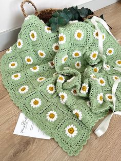 a green crocheted blanket with yellow and white daisies on it next to a basket