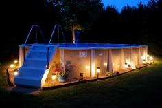 an outdoor swimming pool lit up at night with lights on the side and steps leading to it