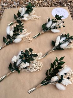 six white flowers and greenery are arranged on a piece of cardboard