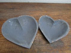 two gray heart shaped dishes sitting on top of a wooden table next to each other