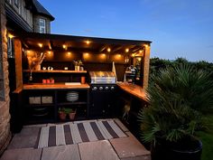 an outdoor kitchen is lit up at night with string lights on the roof and outside