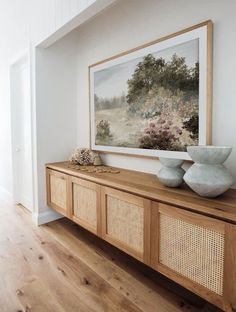 a painting is hanging on the wall next to a wooden shelf with two vases