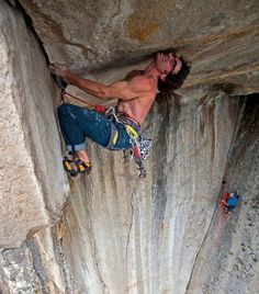 a shirtless man climbing up the side of a rock face with his hands on his hips