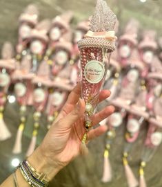 a person holding up a pink glass bottle in front of many other bottles with tassels on them