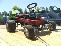 a red cart with four wheels on top of a wooden deck next to other cars