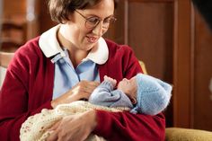 a woman holding a baby in her arms and looking at it's mother, who is wearing a red sweater