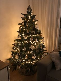 a small christmas tree with white lights in a living room next to a couch and window