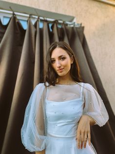 a woman in a white dress standing next to a black curtain with her hands on her hips