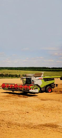 a green and white combine is in the middle of a field with two red combines