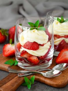 two desserts with strawberries and whipped cream in them on a wooden cutting board