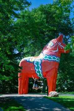 a large red horse statue sitting on top of a lush green park covered in trees