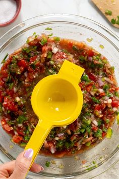 a person holding a yellow spatula in a bowl filled with chopped vegetables and sauce