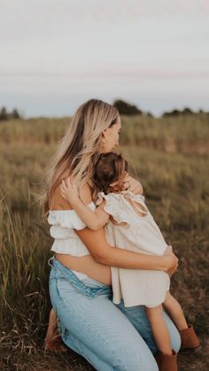 a woman holding a baby in her arms while sitting on the ground with tall grass