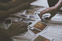 several people are sitting on a bed with polaroid pictures all over the floor and one person is reaching for them