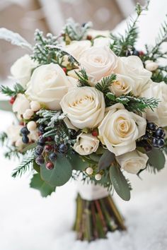 a bridal bouquet with white roses, berries and greenery is sitting in the snow