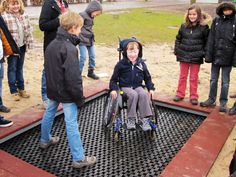 a group of people standing around a little boy in a wheel chair on the ground