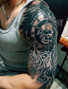 a man with a clock and tree tattoo on his arm is sitting in front of a desk