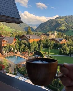 someone is holding a coffee cup in front of a view of the mountains and houses