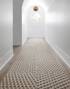 an empty hallway with white walls and beige carpeting on the floor, leading to a round window