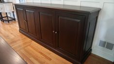 a wooden cabinet sitting on top of a hard wood floor next to a white wall