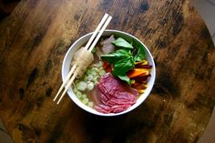 a bowl with meat, vegetables and chopsticks sitting on a wooden table top