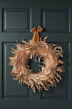 a wreath hanging on the front door of a house with gold bows and feathers attached to it