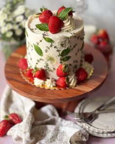 there is a cake with strawberries on the top and white frosting, sitting on a wooden platter