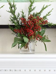 a vase filled with red berries and greenery sitting on top of a white mantle