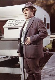 a man in a suit and hat standing next to a trailer