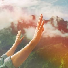 two hands reaching up into the sky with mountains and clouds in the backgroud