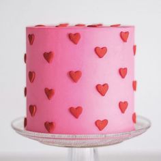 a pink cake with red hearts on it sitting on a glass stand, ready to be eaten