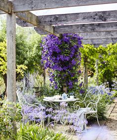 a bench and table in a garden with purple flowers