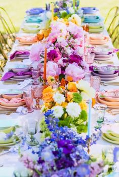 a long table is set with colorful flowers and place settings for an outdoor dinner party