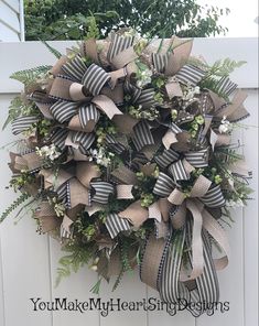 a wreath made out of burlocks and greenery hangs on the side of a white fence