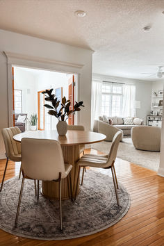 a dining room table with chairs and a vase on top of it in the middle of a living room