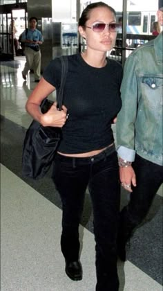 a woman walking through an airport carrying a black handbag and wearing dark colored sunglasses