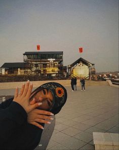 a person wearing a helmet and holding their hand up in front of her face while standing outside