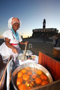 a woman cooking food in a pan on top of a wooden table next to the ocean